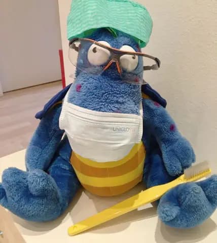 Blaues Plüschtier mit Brille, OP-Maske und Zahnbürste